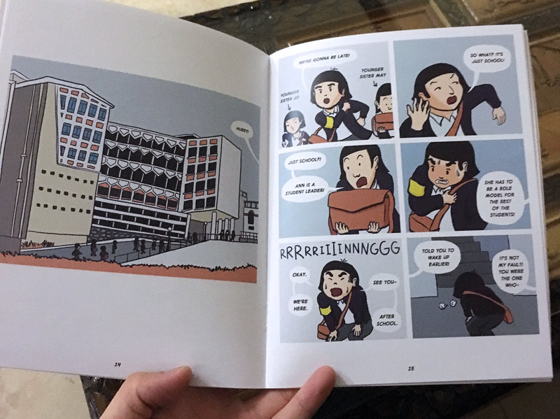 Photo of my hand holding a two-page, full color spread of the printed comic book sample