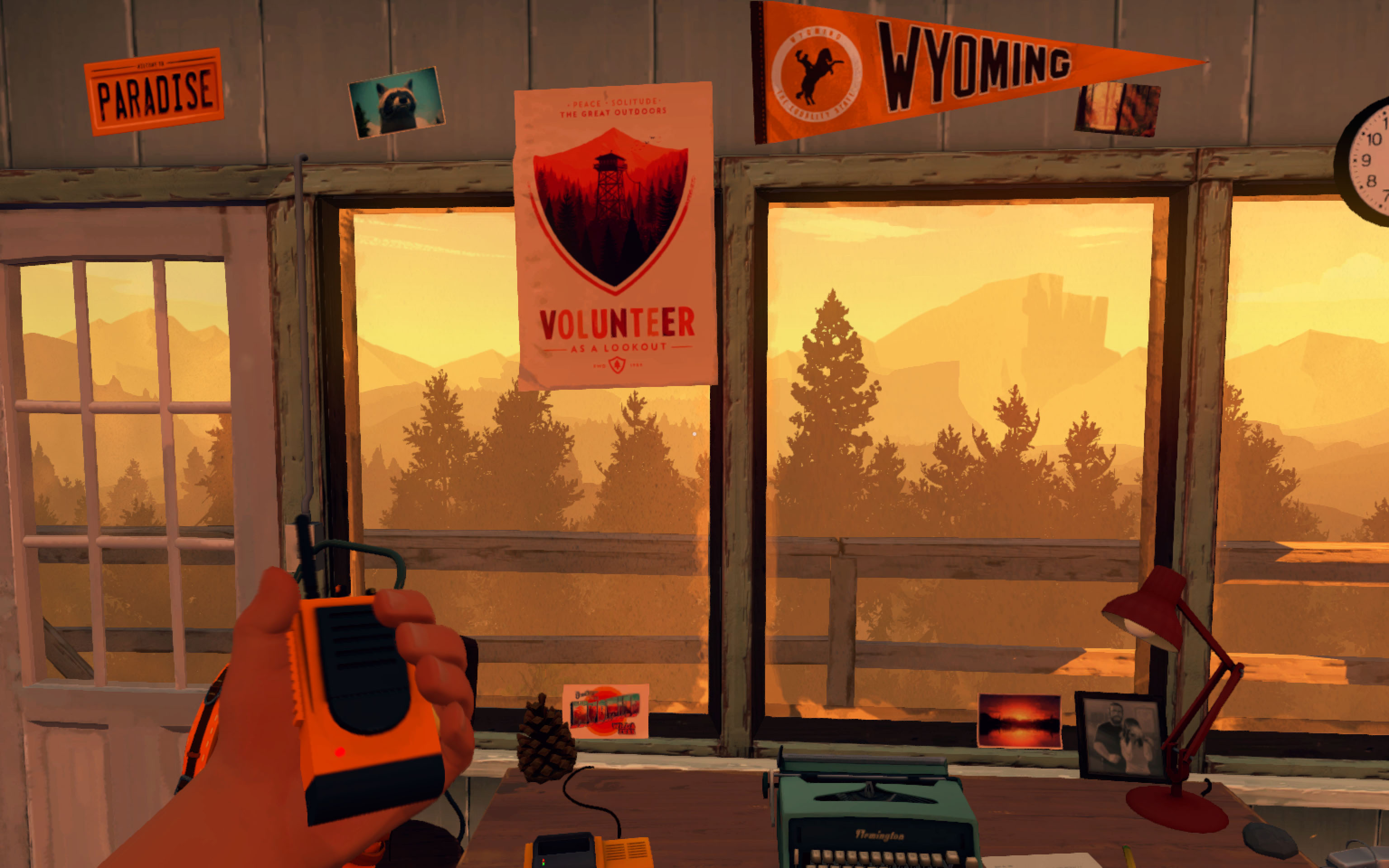 A first person view of a hand holding a yellow walkie talkie staring out at a lush forest in a watch tower cabin with Wyoming penants taped to the wall
